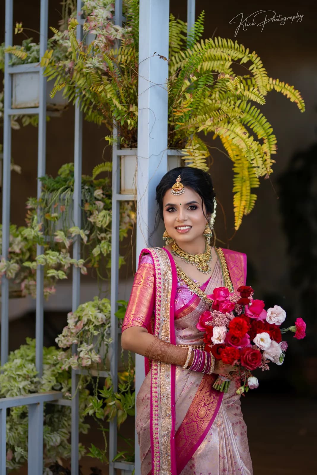 Bride in a pink saree with a bouquet among tropical greenery
