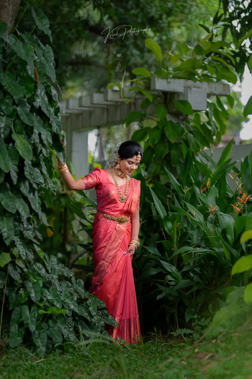 Bride in a coral saree framed by tropical foliage