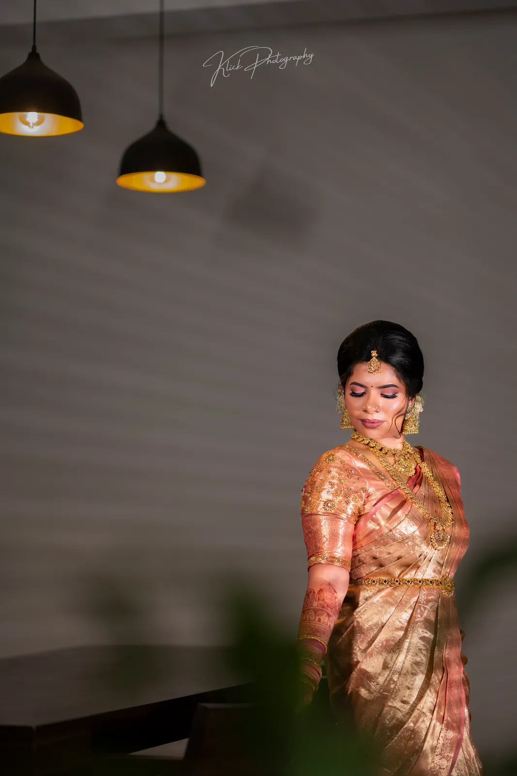 Bride in an orange saree beneath warm pendant lights