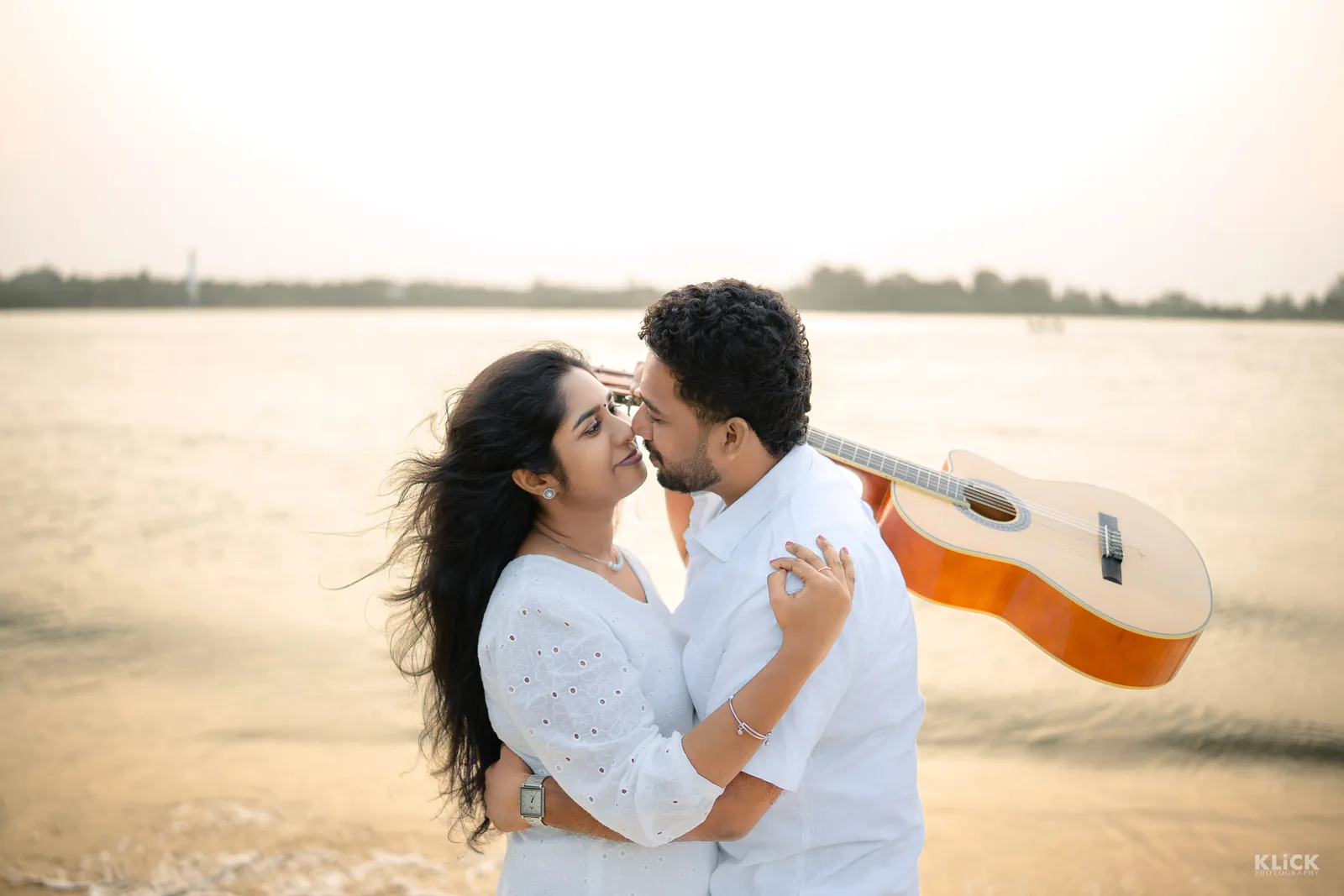 Couple with a guitar by the water at golden hour